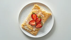 Low Carb Cream Cheese Crepes Low carb cream cheese crepes folded on a white ceramic plate, topped with fresh strawberries and powdered sweetener.