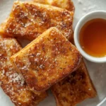 Keto french toast sticks on a white plate dusted with powdered erythritol and served with sugar-free maple syrup