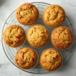 Six golden keto zucchini muffins cooling on a wire rack on a white marble surface.