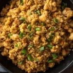 Cauliflower fried rice with chicken in a skillet garnished with green onions and sesame seeds