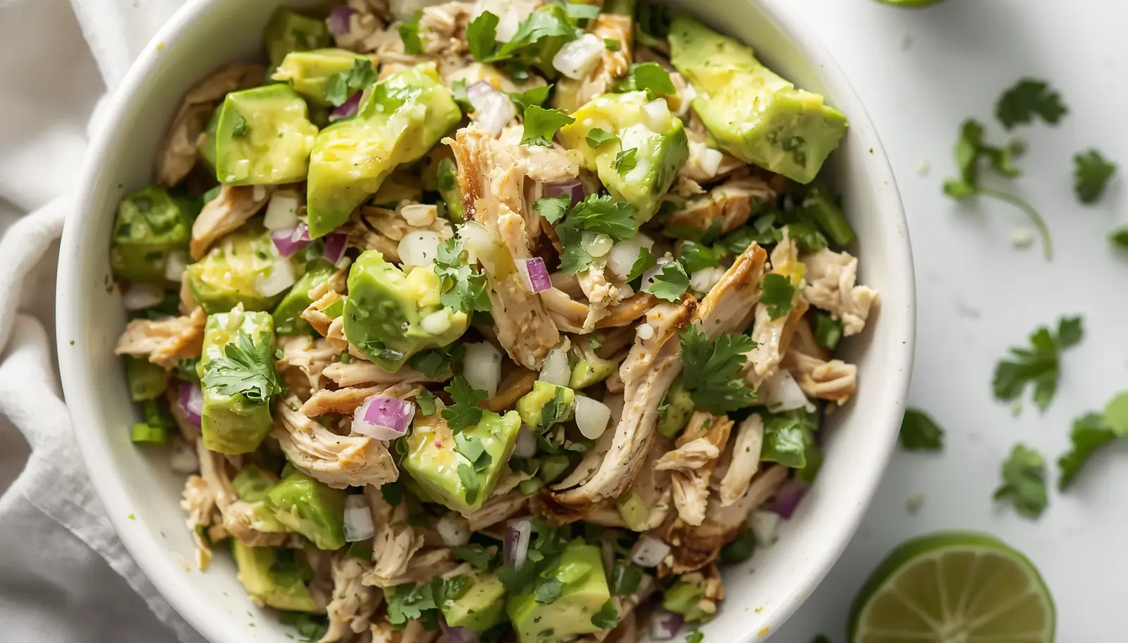 Chicken Avocado Salad 1 Freshly made chicken avocado salad in a white bowl with shredded chicken, cubed avocado, red onion, and cilantro