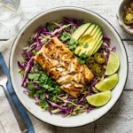 Fish taco slaw recipe bowl with golden seared fish, purple and green cabbage slaw, avocado, and lime wedges