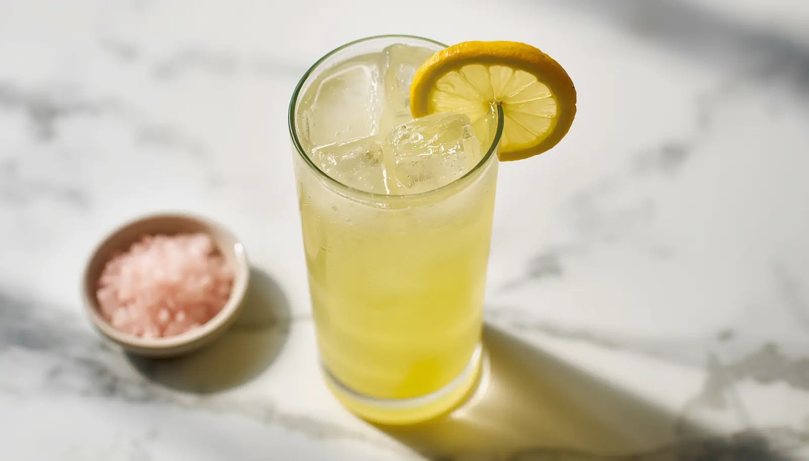 Homemade Electrolyte Drink Recipe 1 Homemade electrolyte drink recipe served in a tall glass with lemon slice and pink Himalayan salt on a marble surface