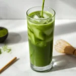 Iced matcha latte recipe served in a tall glass with crushed ice on a white marble surface