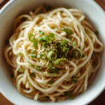 Shirataki noodles recipe served in a white bowl with garlic butter, green onions, and sesame seeds