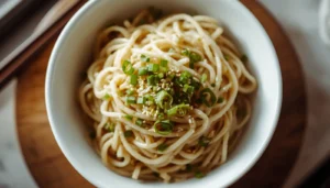 Shirataki noodles recipe served in a white bowl with garlic butter, green onions, and sesame seeds