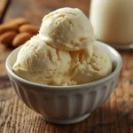 Creamy almond milk ice cream in a bowl with almonds and a pitcher of almond milk