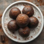 Keto chocolate fat bombs stacked on a white plate with cocoa dusting