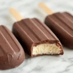 Three keto ice cream bars coated in dark chocolate on a marble countertop