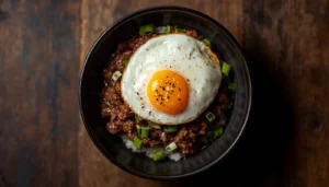 Korean beef bowl recipe with cauliflower rice, fried egg, and sesame seeds in a dark bowl