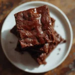 Keto brownies stacked on a white plate showing a fudgy chocolate texture