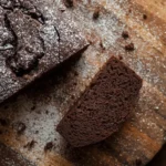 Sliced keto chocolate pound cake on a wooden board dusted with powdered sweetener