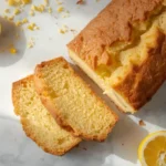 Sliced keto lemon pound cake on a marble counter with fresh lemons